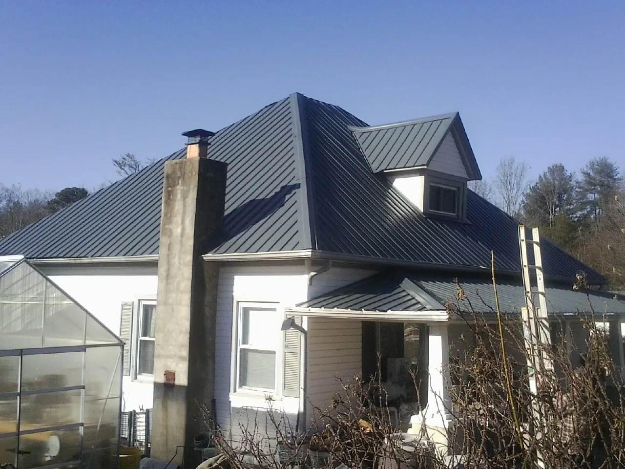 Dark blue standing seam metal roof on a white farmhouse with dormer — Slate & Tile Roof Repair by Roofing Brothers in Bellona