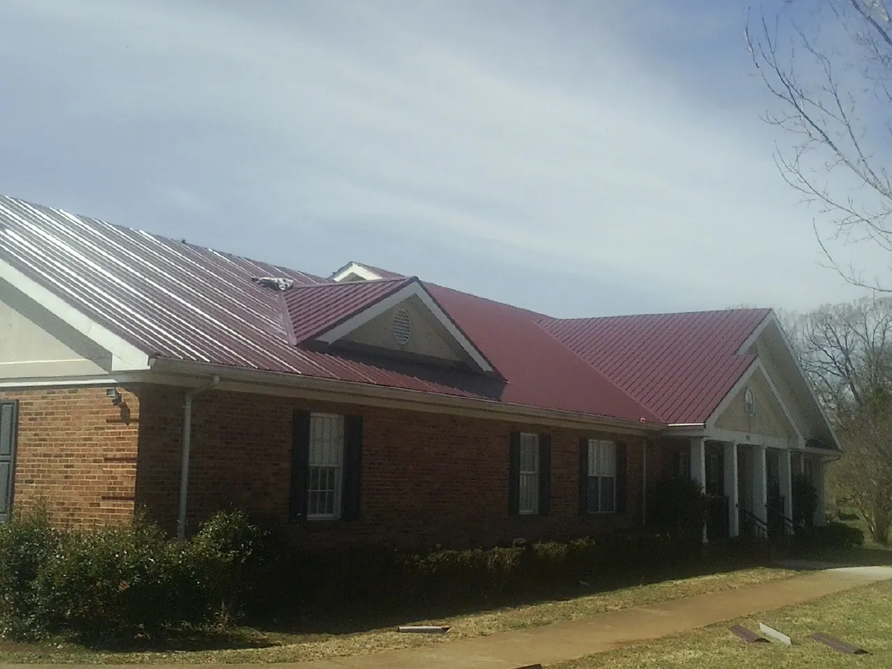 Red metal roof with gabled entries on a long brick building, from a Hail Damage Roof Repair job in Bellona