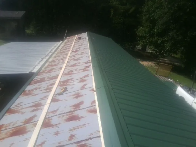 Old rusted panels beside newly installed green metal roofing — Wind Damage Roof Repair by Roofing Brothers in Bellona