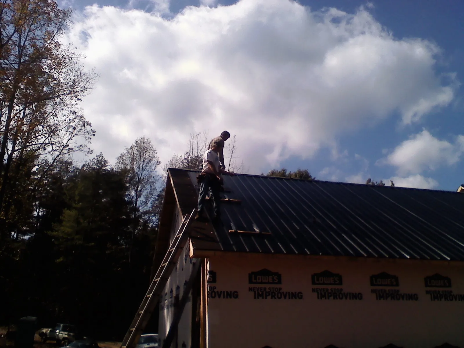 Roofer fastening dark metal panels high against a cloudy sky, from a Roof Inspection job in Bellona