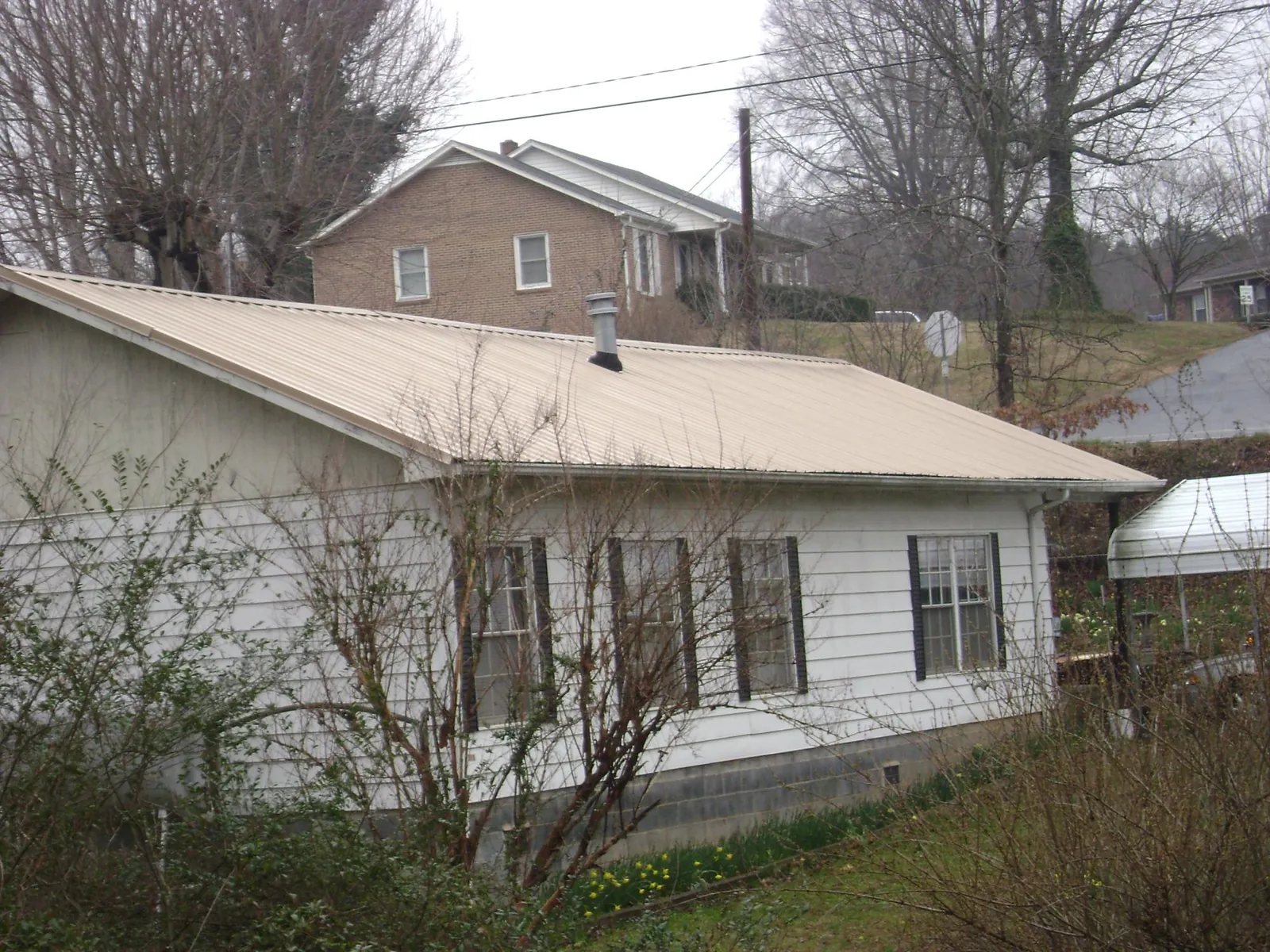 Tan metal roof on a white sided house set into a hillside — Commercial Roofing by Roofing Brothers in Bellona