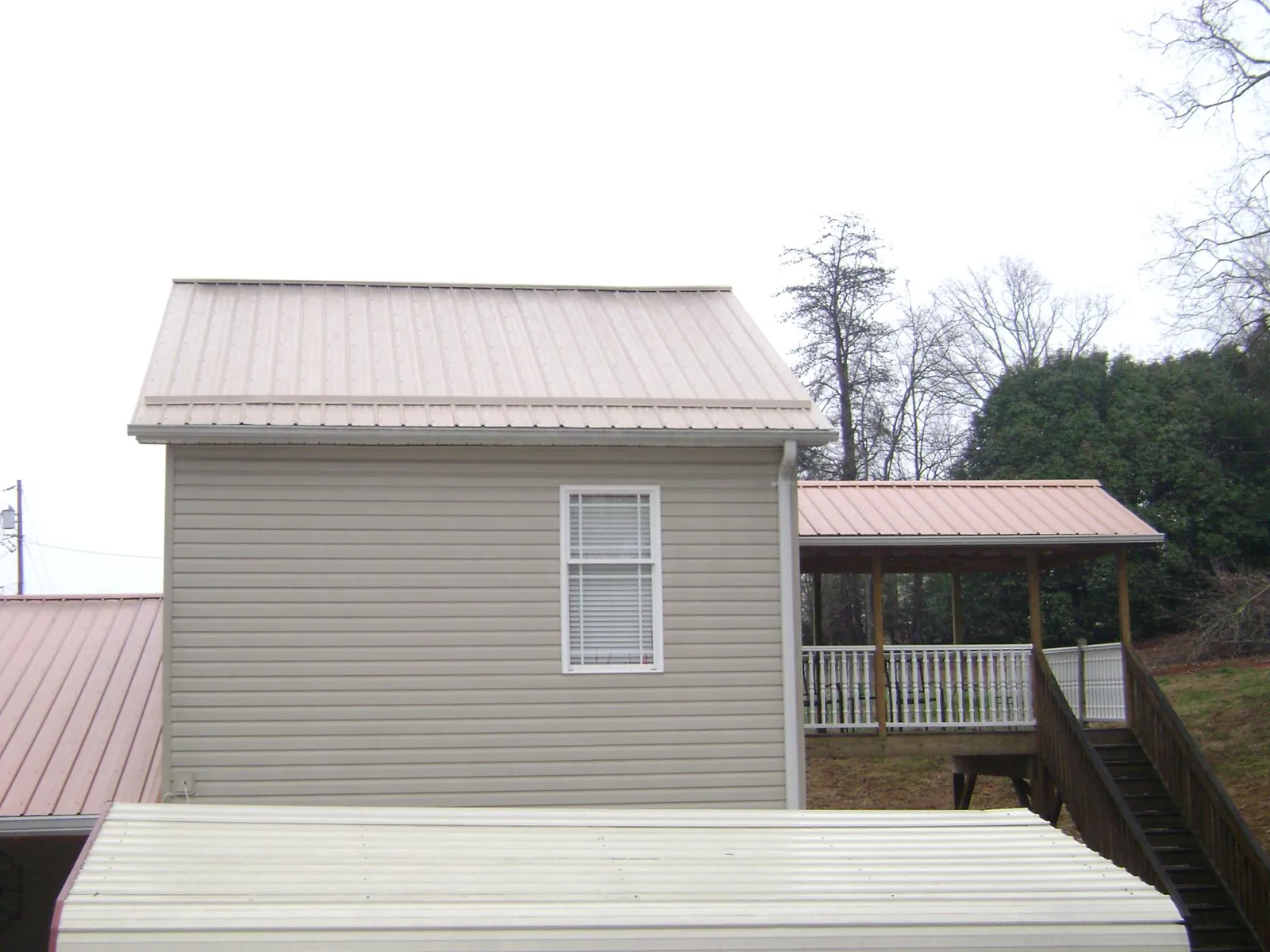 Tan metal roofs on a two story addition and attached porch, from a Roof Replacement job in Bellona